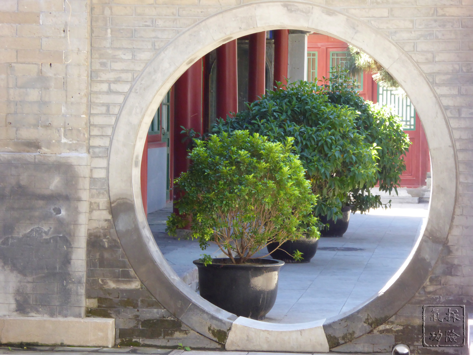 A round entrance in a wall at Beijing's White Cloud Temple reveals another area of the temple decorated with a row of green plants.